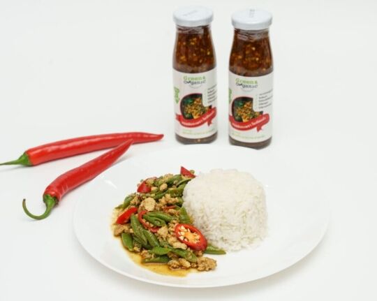 Fermented chili sauce bottles with Thai stir-fry dish and rice, showcasing organic ingredients.